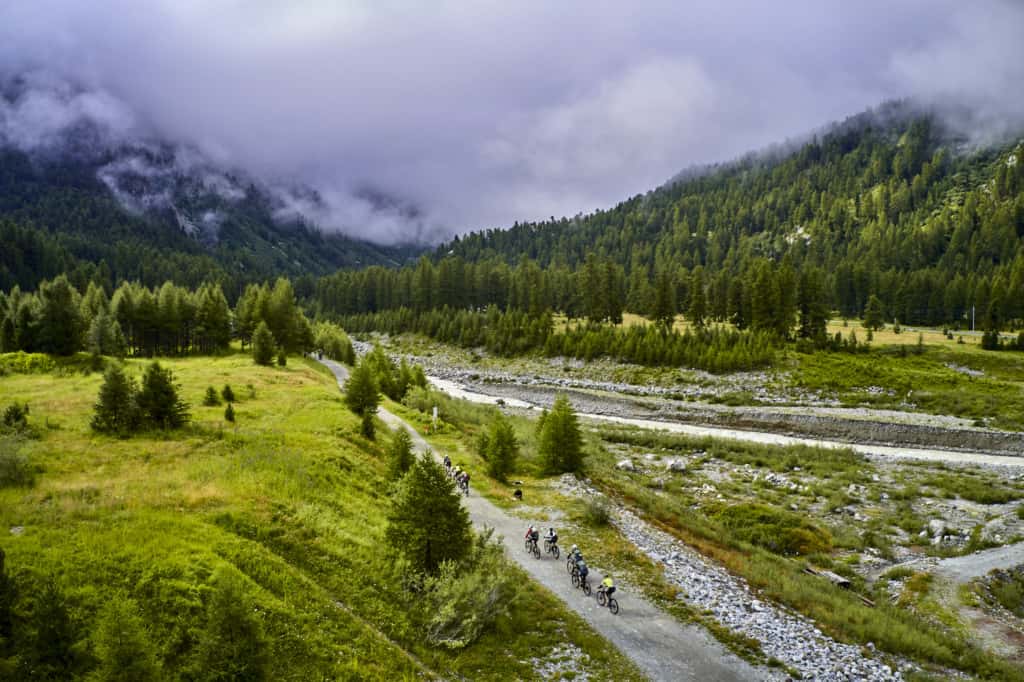 riders beside river with low clouds and mountains ahead